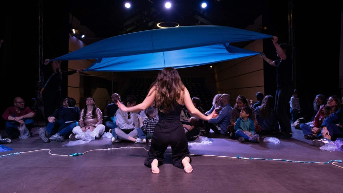 A person on stage facing an audience with their back to the camera. 