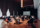 A dozen or so people sitting at socially distanced desks in an ETC hybrid meeting.