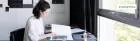 A person working at a table facing a window. 