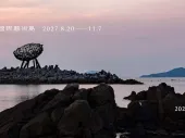 Title of the call on a photo of an artwork perched on rocks beside the sea. 