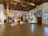 Two people in a gallery exhibition, handling an object that looks like a puppet. 