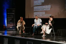 Three people on stage, seated, talking. 