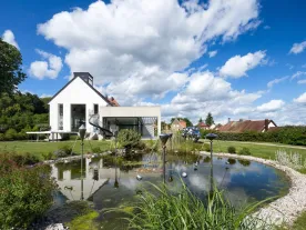 A white, one-story building surrounded by a landscaped garden with a pond and sculptures. 